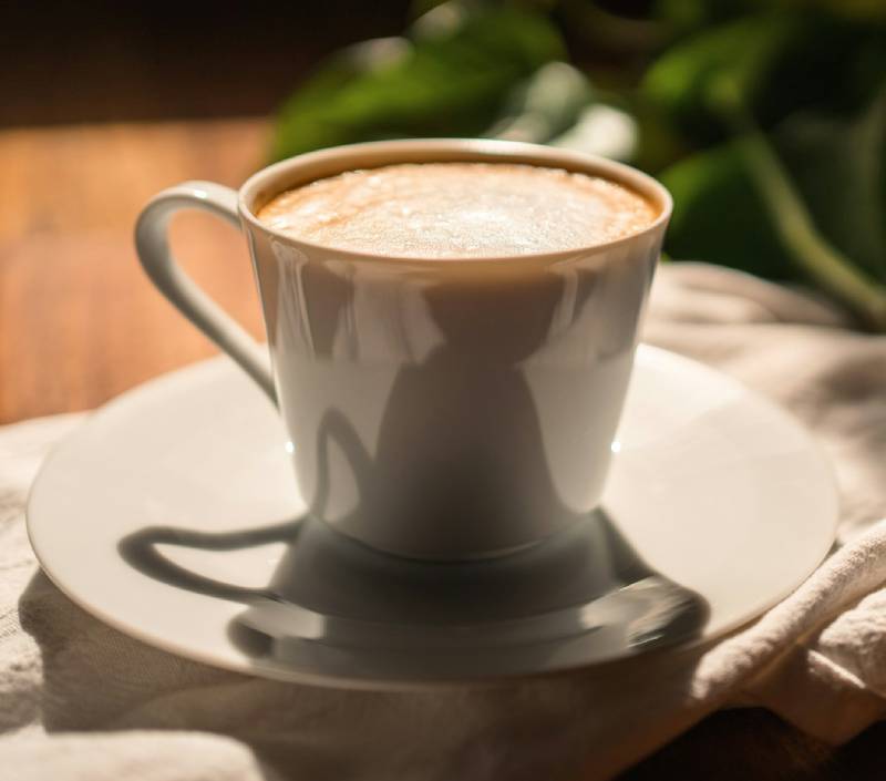 Biała filiżanka kawy na spodku w słońcu