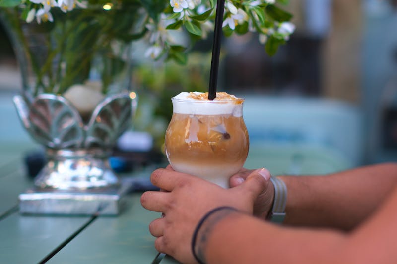 Szklanka mrożonej kawy ze słomką trzymana w dłoniach